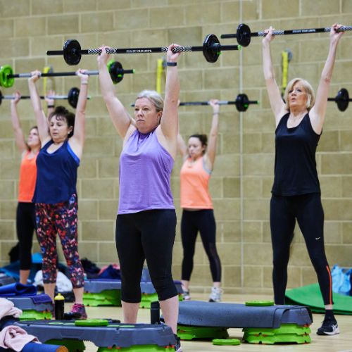 5 women doing a workout class with barbells