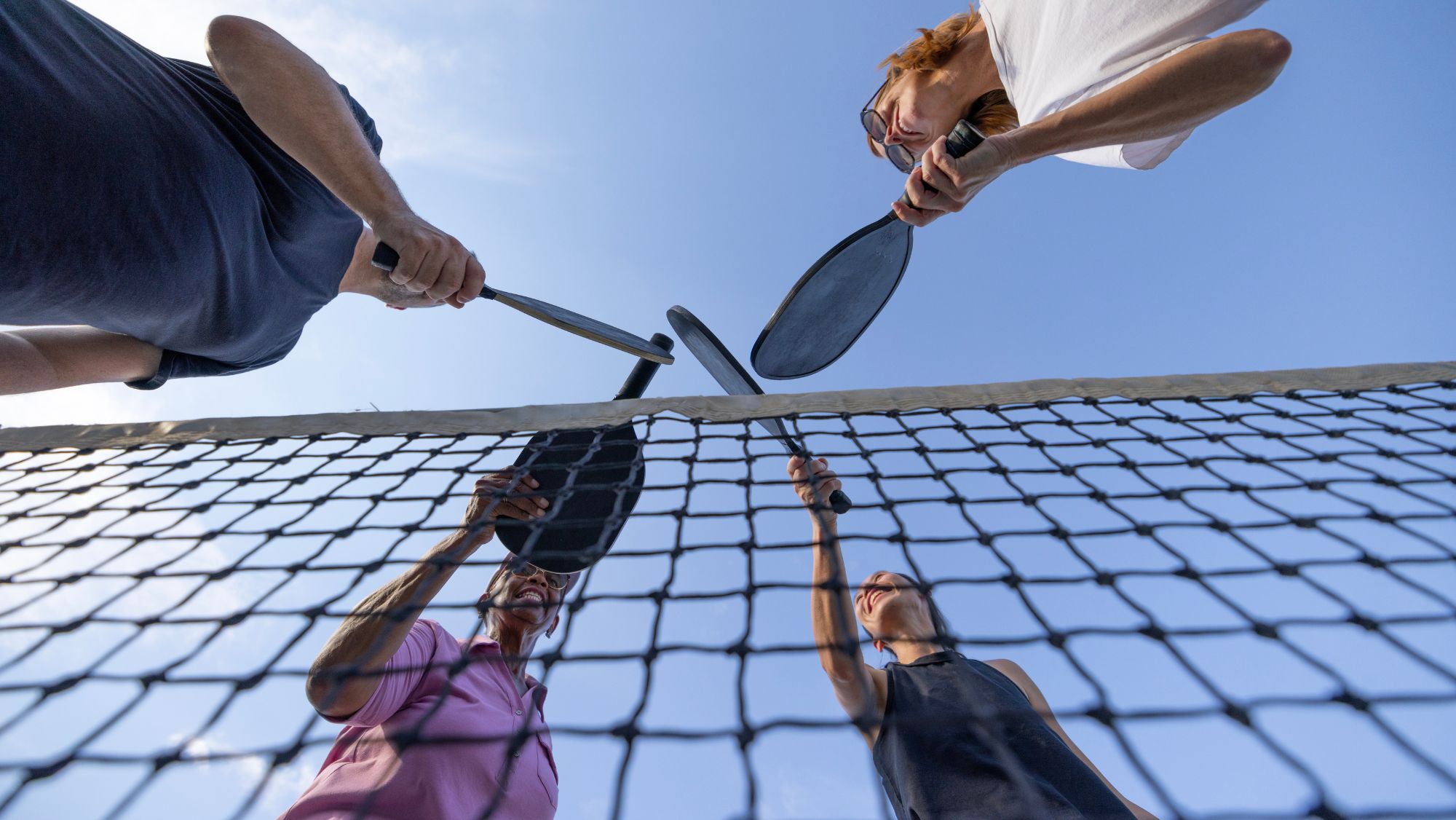 Four pickleball players with their paddles above the net