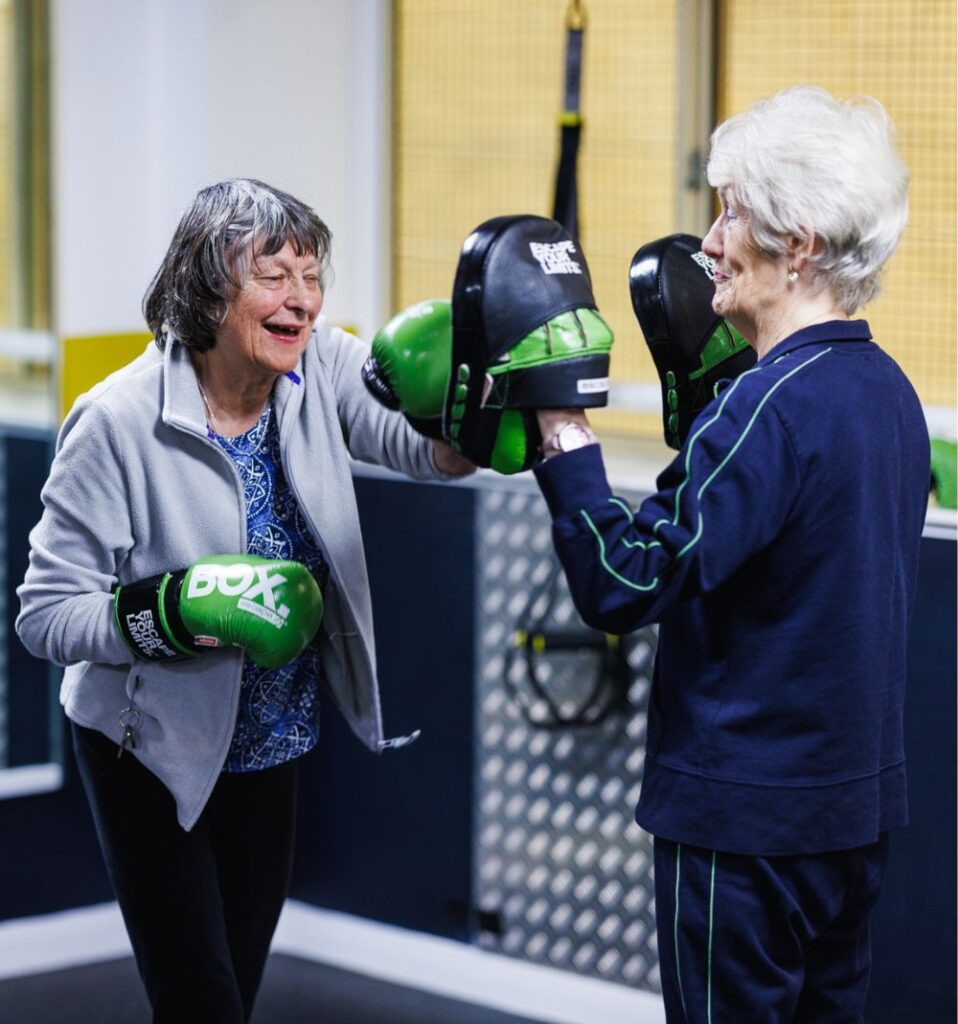 two elderly women exercising with boxing pads in a gym