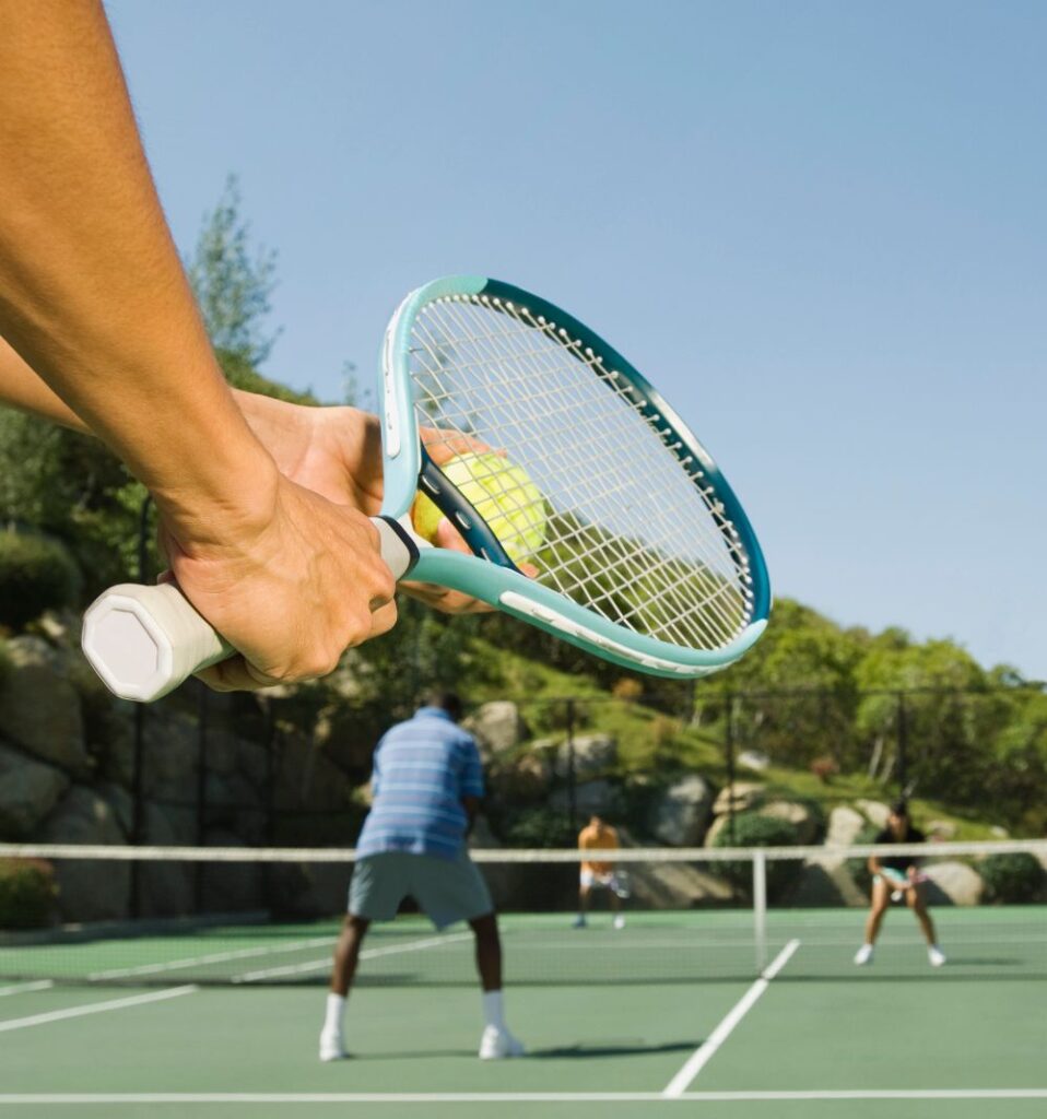 person preparing to serve in tennis with other players on court in the background