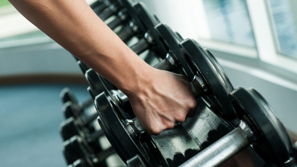 person picking up dumbbells from dumbbell rack