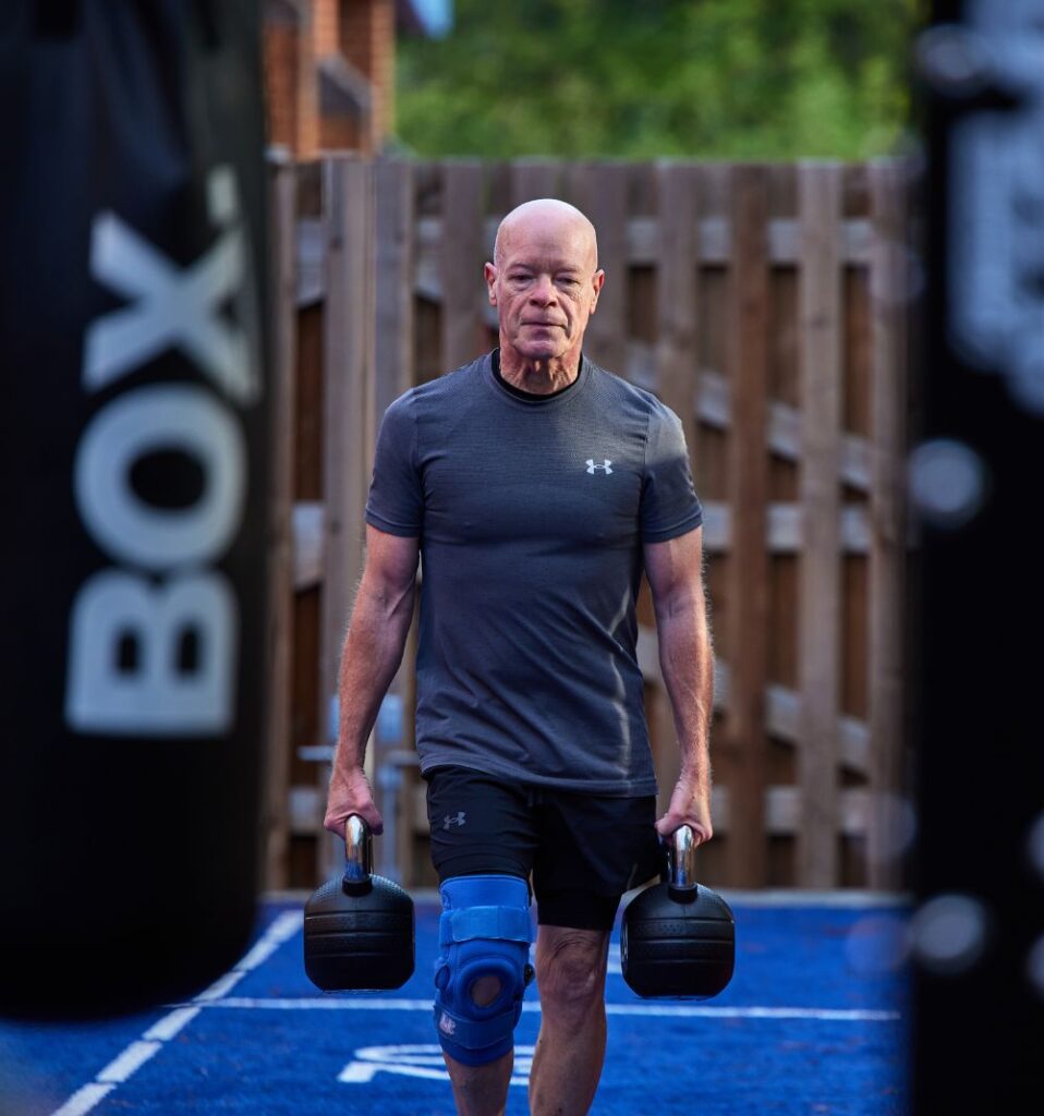 man doing a farmers carry with kettlebells in outdoor fitness yard