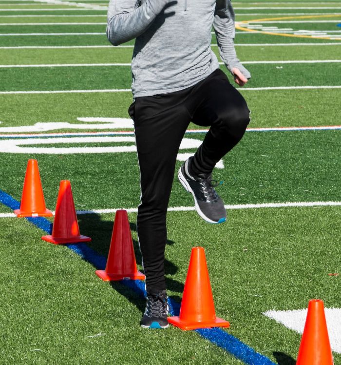 person practising high knees with cones on athletics track